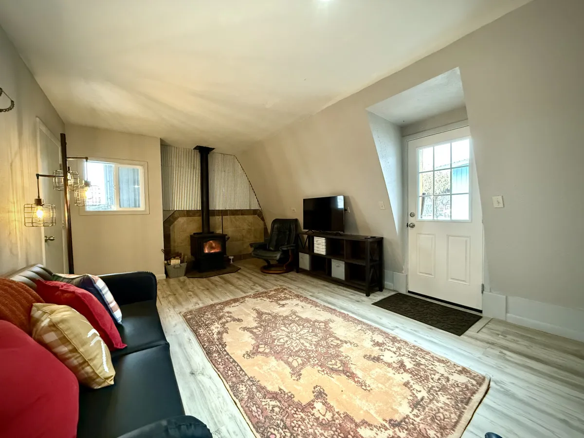 A welcoming living space featuring a wood-burning stove, a sofa adorned with colorful cushions, a soft rug, and a TV stand with a flat-screen TV. The open arrangement encourages both relaxation and socializing.