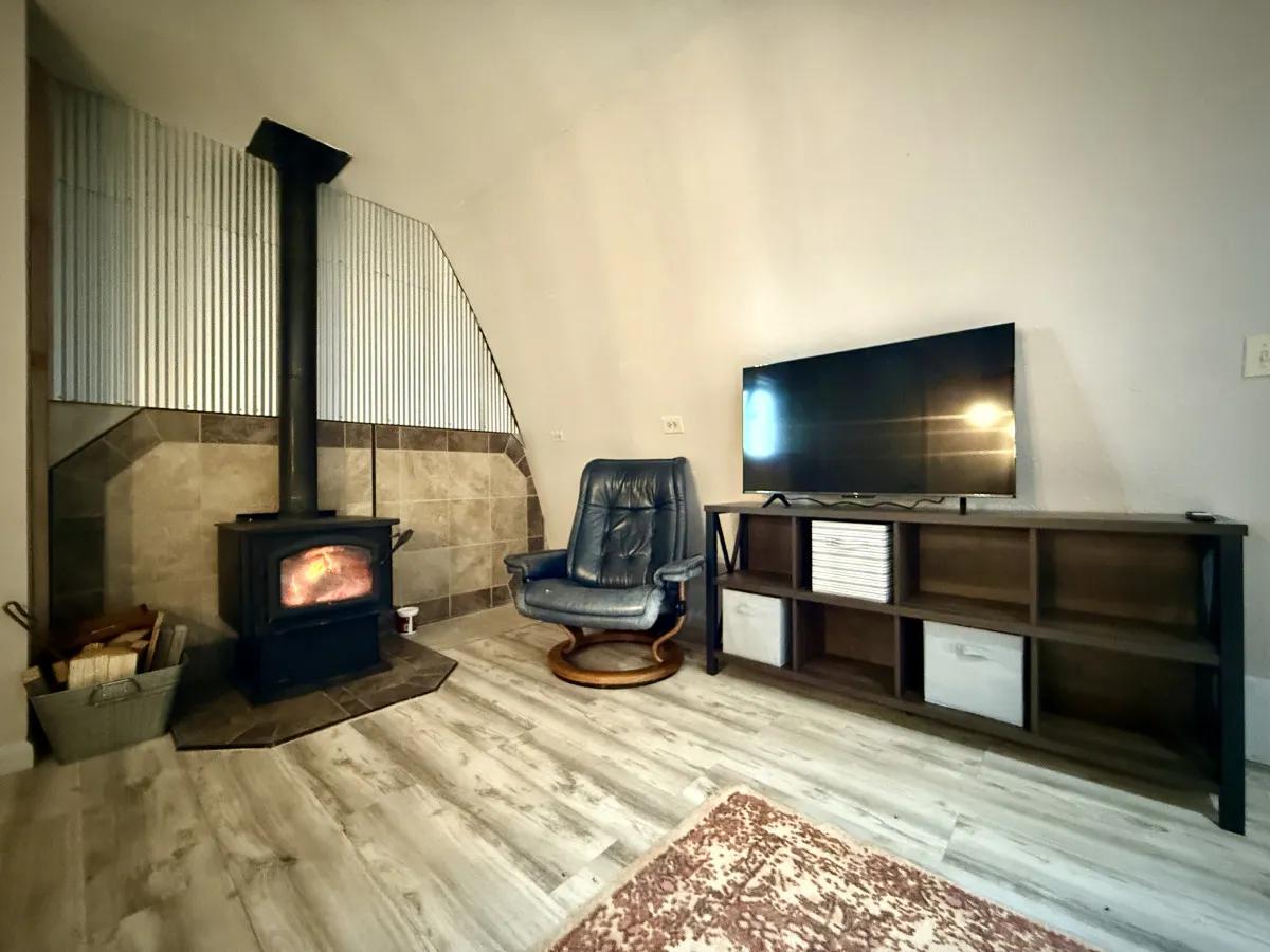 A charming corner of the living room with a wood-burning stove, a classic blue rocking chair, a television, and a shelf unit filled with books and decor. The setup balances warmth and relaxation, perfect for quiet evenings in.